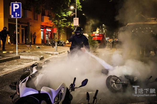Un agente de los Mossos sofoca el fuego bajo el que prendían varias motocicletas en Gràcia. / AFP PHOTO / STR